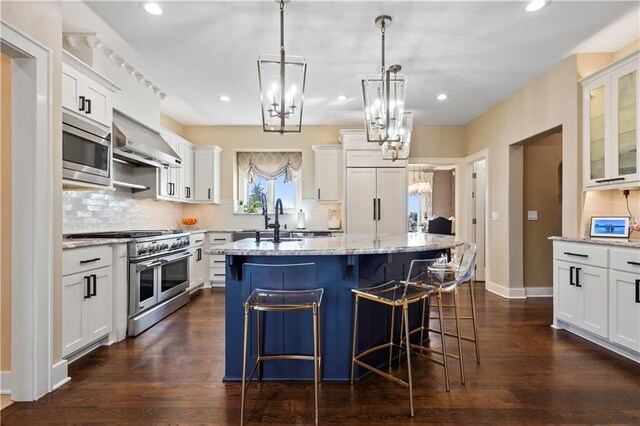 20711 Benson St, Bucyrus, KS 66013 - kitchen with built in appliances, wall chimney exhaust hood, an island with sink, a chandelier, and light stone countertops