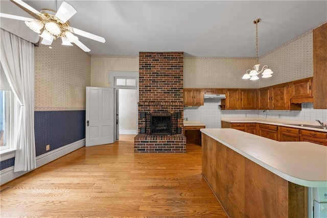 5322 SE Riverside Ter, Saint Joseph, MO 64507 - kitchen with wallpapered walls, brown cabinetry, a sink, light wood-style flooring, and a ceiling fan