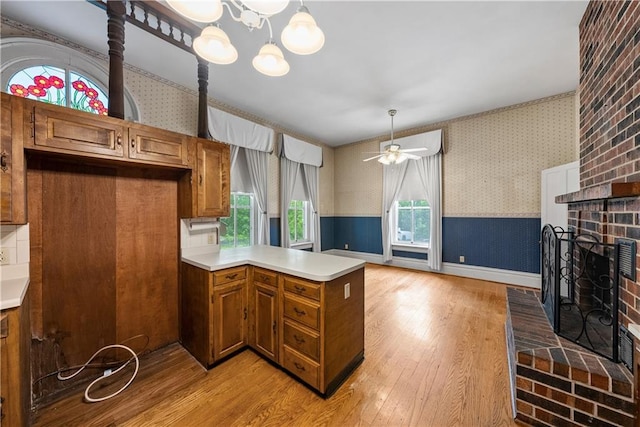 5322 SE Riverside Ter, Saint Joseph, MO 64507 - kitchen featuring wallpapered walls, brown cabinets, light wood-type flooring, a peninsula, and light countertops