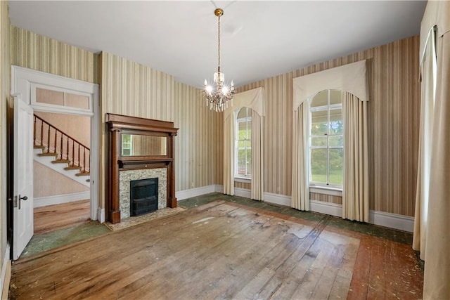 5322 SE Riverside Ter, Saint Joseph, MO 64507 - unfurnished living room featuring wallpapered walls, a stone fireplace, a chandelier, baseboards, and wood-type flooring