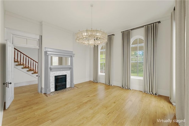5322 SE Riverside Ter, Saint Joseph, MO 64507 - unfurnished living room with light wood-type flooring, a tile fireplace, a chandelier, stairs, and crown molding