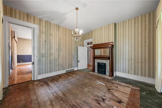 5322 SE Riverside Ter, Saint Joseph, MO 64507 - unfurnished living room featuring wallpapered walls, a chandelier, wood-type flooring, a fireplace with flush hearth, and baseboards