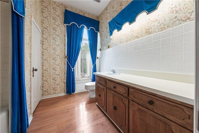 5322 SE Riverside Ter, Saint Joseph, MO 64507 - bathroom with wallpapered walls, wood-type flooring, toilet, vanity, and shower / tub combo with curtain