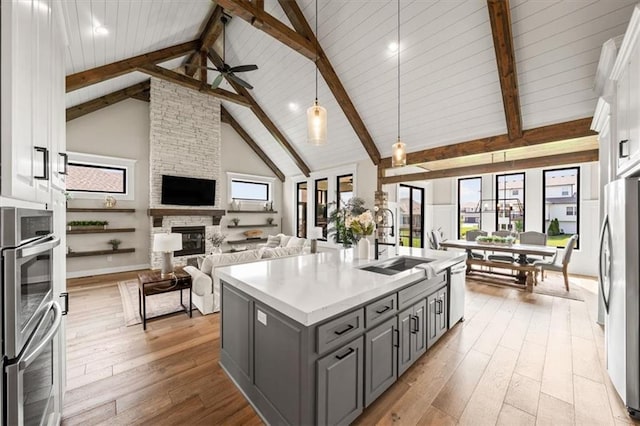 3053 NW Thoreau Ln, Lees Summit, MO 64081 - kitchen featuring gray cabinetry, stainless steel appliances, open floor plan, a stone fireplace, and white cabinetry