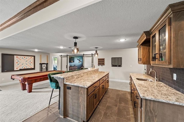 3053 NW Thoreau Ln, Lees Summit, MO 64081 - kitchen with a barn door, glass insert cabinets, light stone counters, a breakfast bar area, and a textured ceiling