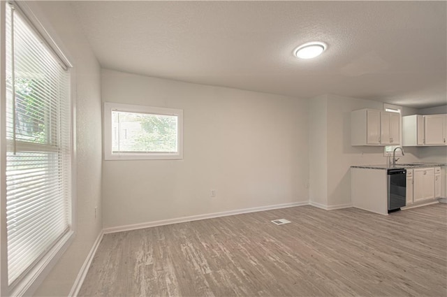 3874 E 63rd St, Kansas City, MO 64130 - kitchen featuring black dishwasher, light wood-style floors, healthy amount of natural light, a textured ceiling, and white cabinets