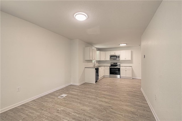 3874 E 63rd St, Kansas City, MO 64130 - kitchen with stainless steel appliances, light wood finished floors, white cabinets, light countertops, and a textured ceiling