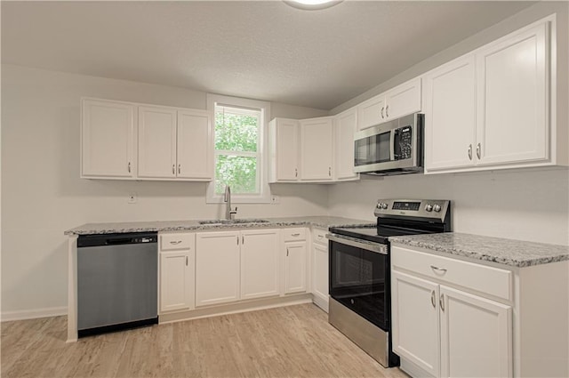 3874 E 63rd St, Kansas City, MO 64130 - kitchen with appliances with stainless steel finishes, light wood-type flooring, white cabinets, light stone counters, and a textured ceiling