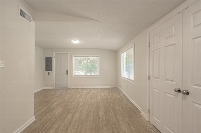 3874 E 63rd St, Kansas City, MO 64130 - empty room with electric panel, vaulted ceiling, light wood-style flooring, and a textured ceiling