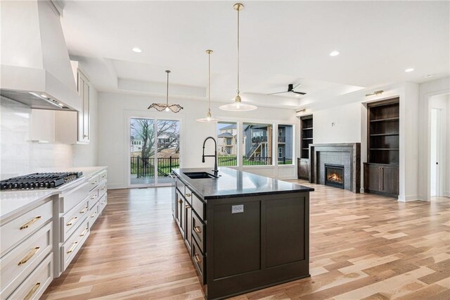 12445 Empress St, Platte City, MO 64079 - kitchen with wall chimney range hood, stainless steel gas cooktop, a sink, a tray ceiling, and light wood-style flooring