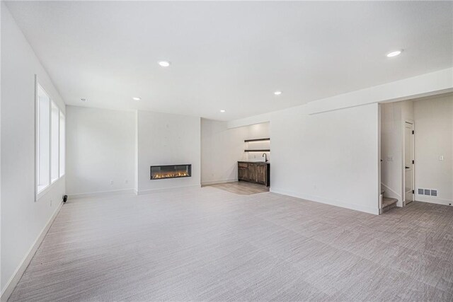 12445 Empress St, Platte City, MO 64079 - unfurnished living room with light carpet, a glass covered fireplace, recessed lighting, baseboards, and stairs