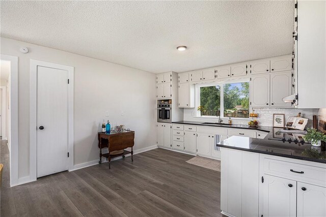 624 S Locust St, Gardner, KS 66030 - kitchen with oven, dark countertops, dark wood-type flooring, white cabinets, and a textured ceiling