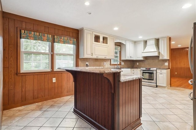 126 W 116th St, Kansas City, MO 64114 - kitchen with stainless steel appliances, premium range hood, wood walls, light stone countertops, and decorative backsplash
