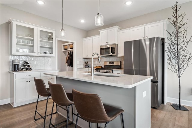 9504 N Amoret Ave, Kansas City, MO 64154 - kitchen with appliances with stainless steel finishes, decorative backsplash, white cabinets, light wood-style flooring, and a kitchen breakfast bar