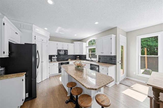 17631 S Brockway St, Olathe, KS 66062 - kitchen featuring black appliances, a kitchen island, a kitchen breakfast bar, wood finished floors, and a textured ceiling