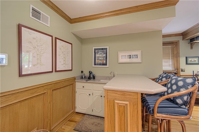 301 W 109th St, Kansas City, MO 64114 - kitchen with a peninsula, crown molding, a breakfast bar, light wood-style floors, and light countertops