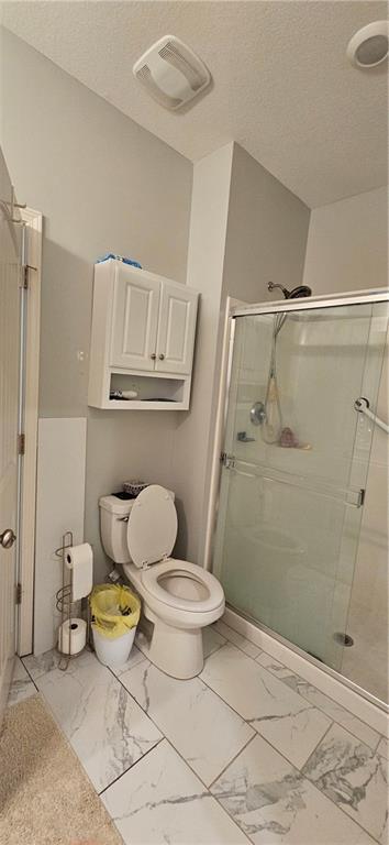 12432 Live Oak Cir, Peculiar, MO 64078 - bathroom featuring marble finish flooring, toilet, a shower stall, and a textured ceiling