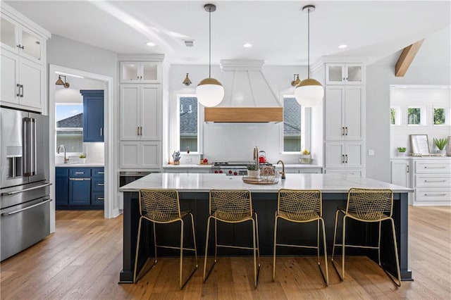 9291 Brownridge St, Lenexa, KS 66220 - kitchen with high end fridge, custom range hood, tasteful backsplash, a kitchen island with sink, and light wood-style floors