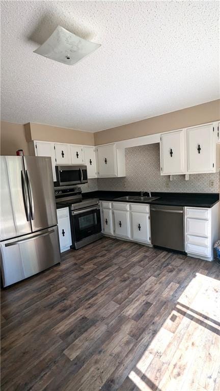 8476 Lane Dr, Raytown, MO 64138 - kitchen with appliances with stainless steel finishes, a textured ceiling, white cabinetry, dark countertops, and dark wood finished floors