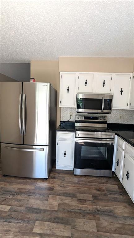 8476 Lane Dr, Raytown, MO 64138 - kitchen featuring appliances with stainless steel finishes, dark countertops, a textured ceiling, white cabinetry, and dark wood-style flooring