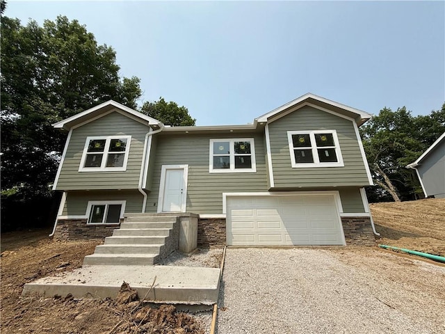 134 Cedar Cir, Warrensburg, MO 64093 - split foyer home featuring a garage, gravel driveway, and stone siding