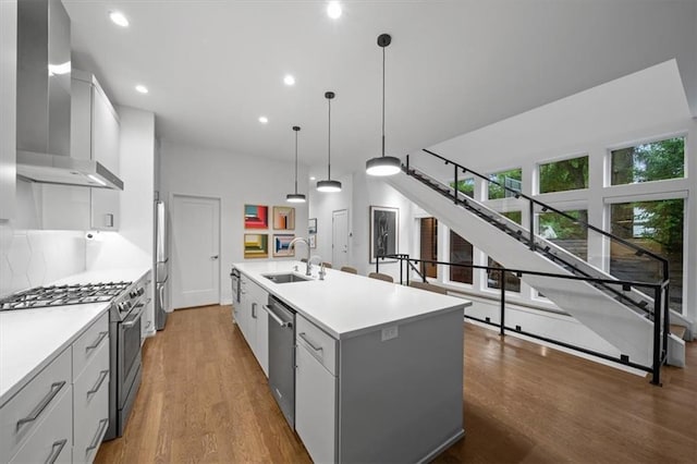 2711 W 49th St, Westwood, KS 66205 - kitchen featuring appliances with stainless steel finishes, wall chimney range hood, a sink, an island with sink, and wood finished floors