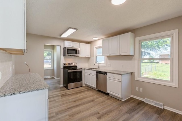 105 S W St, Concordia, MO 64020 - kitchen with appliances with stainless steel finishes, white cabinets, light wood-style floors, plenty of natural light, and a textured ceiling