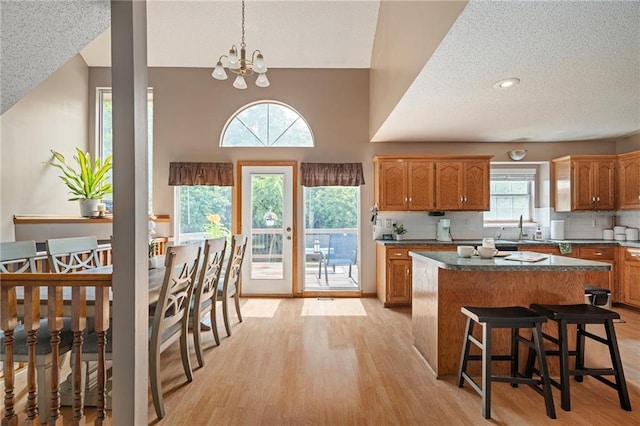 1229 SE Princeton Dr, Lees Summit, MO 64081 - kitchen with light wood finished floors, brown cabinets, a center island, a textured ceiling, and decorative backsplash