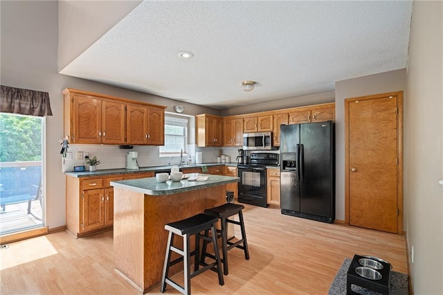 1229 SE Princeton Dr, Lees Summit, MO 64081 - kitchen featuring black appliances, light wood finished floors, a center island, decorative backsplash, and a textured ceiling