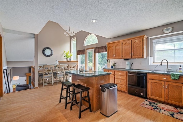 1229 SE Princeton Dr, Lees Summit, MO 64081 - kitchen with black dishwasher, a textured ceiling, light wood-style floors, a center island, and a kitchen bar