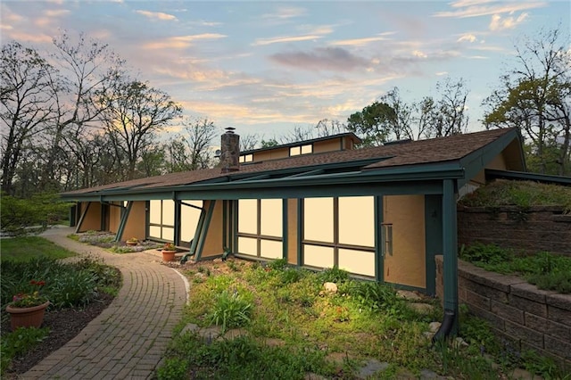 19913 Pepper Tree Rd, Edgerton, KS 66021 - back of house at dusk featuring a chimney, stucco siding, and roof with shingles
