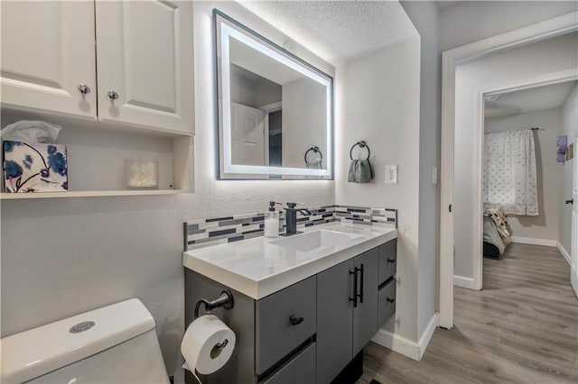 604 Lake Rd, Garden City, MO 64747 - ensuite bathroom with vanity, wood finished floors, toilet, decorative backsplash, and baseboards