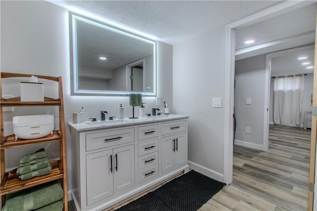 604 Lake Rd, Garden City, MO 64747 - bathroom featuring double vanity, wood finished floors, baseboards, a textured ceiling, and recessed lighting