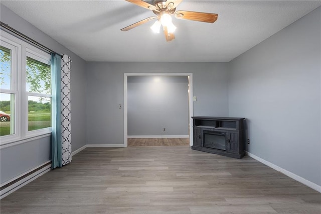 10203 Outer Rd, Odessa, MO 64076 - unfurnished living room with a baseboard heating unit, light wood-style flooring, a fireplace, and a ceiling fan