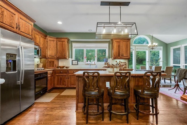 14810 W 72nd St, Shawnee, KS 66216 - kitchen with stainless steel appliances, brown cabinetry, a center island, a chandelier, and healthy amount of natural light