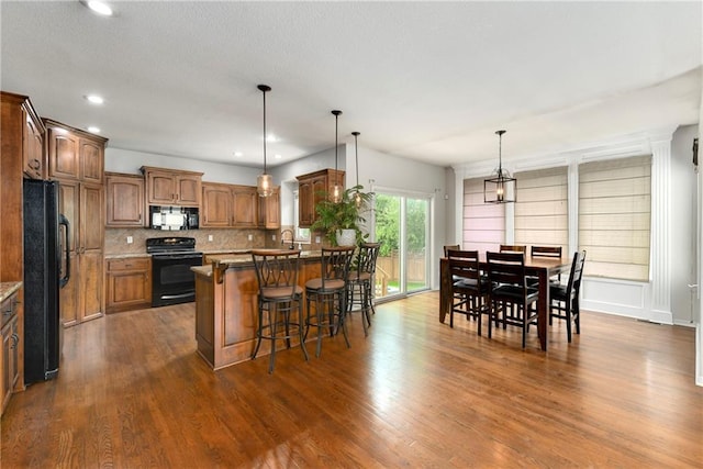 21835 W 175th Ter, Olathe, KS 66062 - kitchen with black appliances, a kitchen breakfast bar, decorative backsplash, a peninsula, and dark wood-type flooring