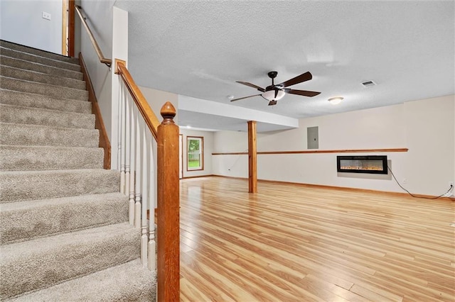8604 NE 72nd Ter, Kansas City, MO 64158 - unfurnished living room featuring wood finished floors, stairway, a glass covered fireplace, and a textured ceiling