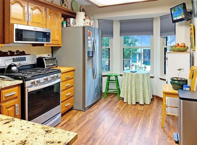 305 E Partridge Ave, Independence, MO 64055 - kitchen with stainless steel appliances, light wood-type flooring, brown cabinets, and light stone countertops