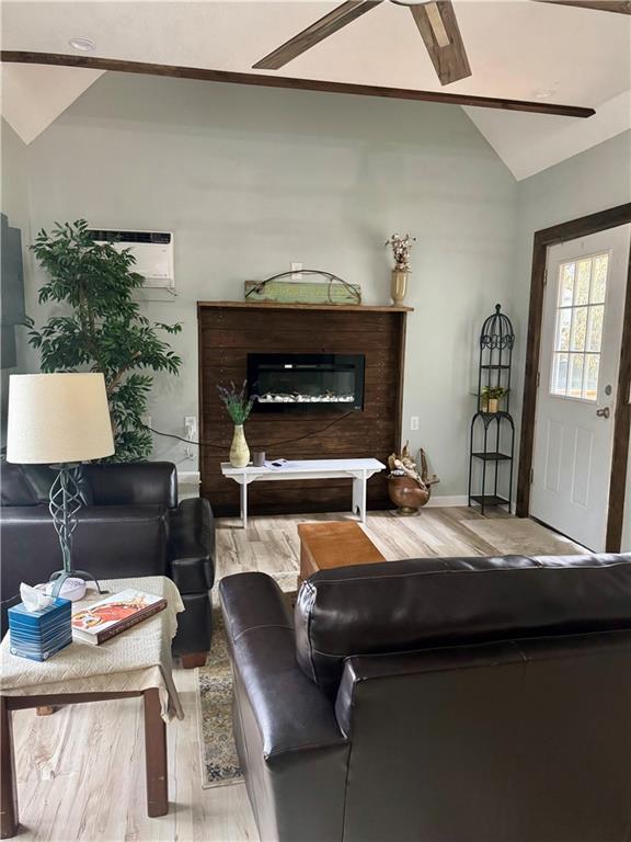 10057 Otter Rd, Clinton, MO 64735 - living area with wood finished floors, lofted ceiling, a glass covered fireplace, baseboards, and an AC wall unit