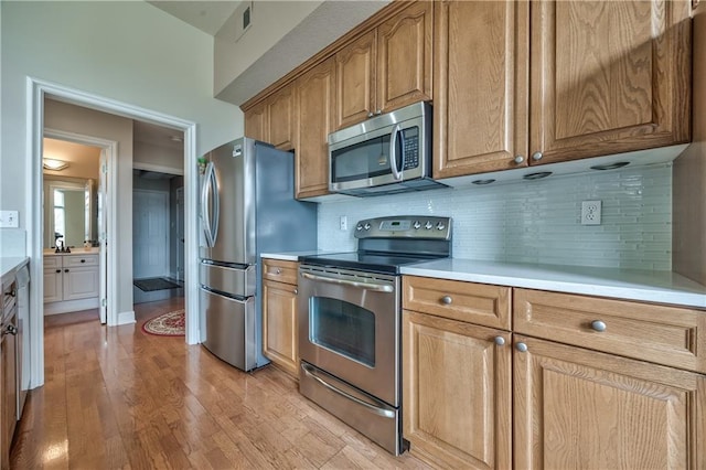 12207 England St, Overland Park, KS 66213 - kitchen featuring appliances with stainless steel finishes, light countertops, light wood-style flooring, and tasteful backsplash