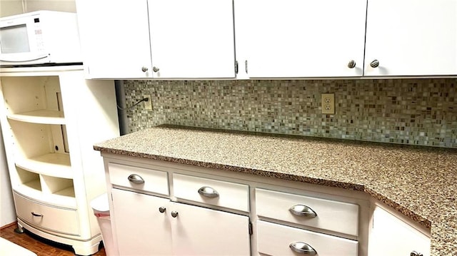1441 S Maple St, Ottawa, KS 66067 - detailed view of white microwave, white cabinets, decorative backsplash, and light stone counters