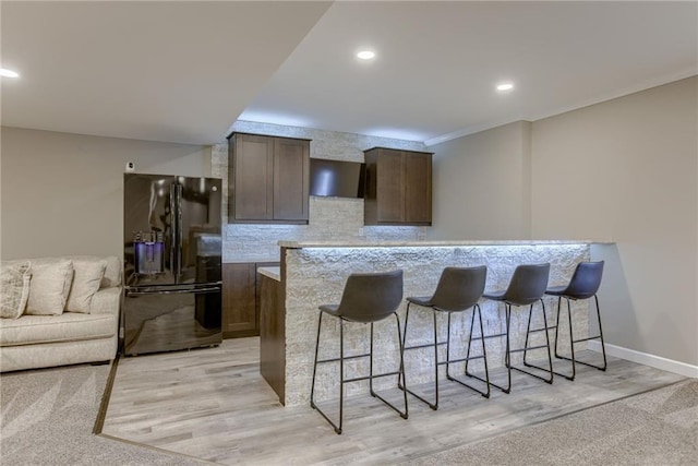 8721 N Mersington Ave, Kansas City, MO 64156 - kitchen with black fridge, a breakfast bar area, extractor fan, dark brown cabinets, and backsplash