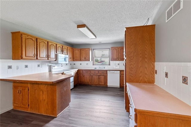12 SW 365th Rd, Warrensburg, MO 64093 - kitchen with white appliances, a peninsula, brown cabinets, a textured ceiling, and dark wood-style floors