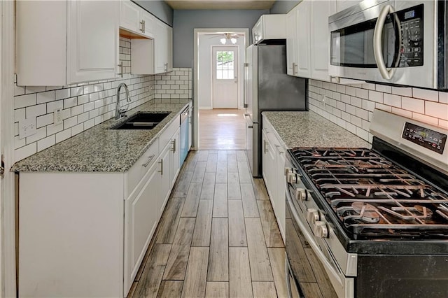 7907 Elm Ave, Raytown, MO 64138 - kitchen with stainless steel appliances, white cabinets, light wood-style flooring, light stone countertops, and a ceiling fan