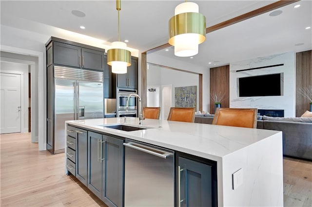 15601 Catalina St, Overland Park, KS 66224 - kitchen with appliances with stainless steel finishes, a sink, a kitchen island with sink, hanging light fixtures, and light wood finished floors