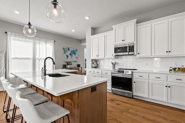 1517 SW Arbor Creek Dr, Lees Summit, MO 64082 - kitchen featuring stainless steel appliances, a sink, light wood finished floors, backsplash, and a center island with sink