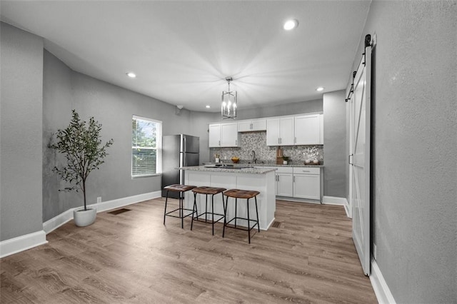 3332 Flora Ave, Kansas City, MO 64109 - kitchen with freestanding refrigerator, a barn door, a center island, white cabinets, and decorative backsplash