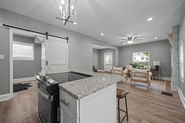 3332 Flora Ave, Kansas City, MO 64109 - kitchen with black electric range, a barn door, a kitchen island, a kitchen bar, and open floor plan