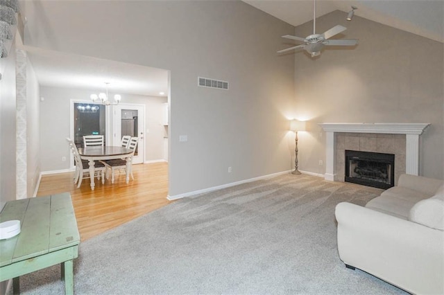 7503 N Lewis Ave, Kansas City, MO 64158 - carpeted living area featuring a chandelier, high vaulted ceiling, a tiled fireplace, a ceiling fan, and wood finished floors