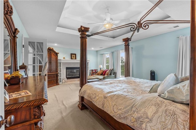 4022 SW Flintrock Dr, Lees Summit, MO 64082 - bedroom with carpet flooring, a tray ceiling, a glass covered fireplace, decorative columns, and a ceiling fan